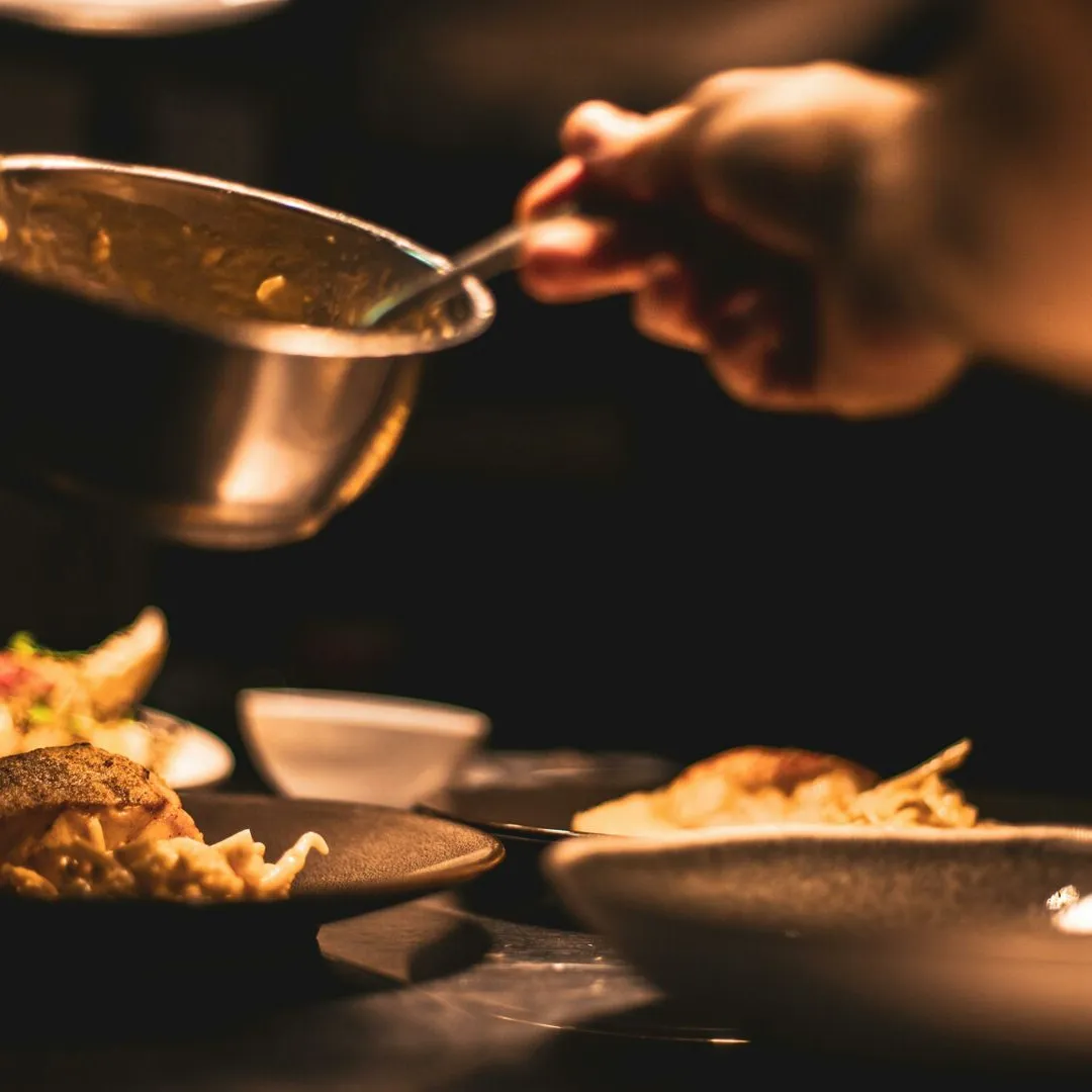 Gourmet dish being plated by a chef in a dimly lit restaurant's kitchen.
