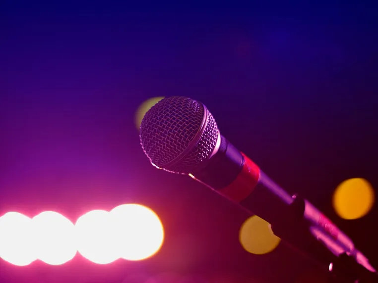 Colorful stage lighting highlights a microphone in a close-up view, perfect for music and performance themes.