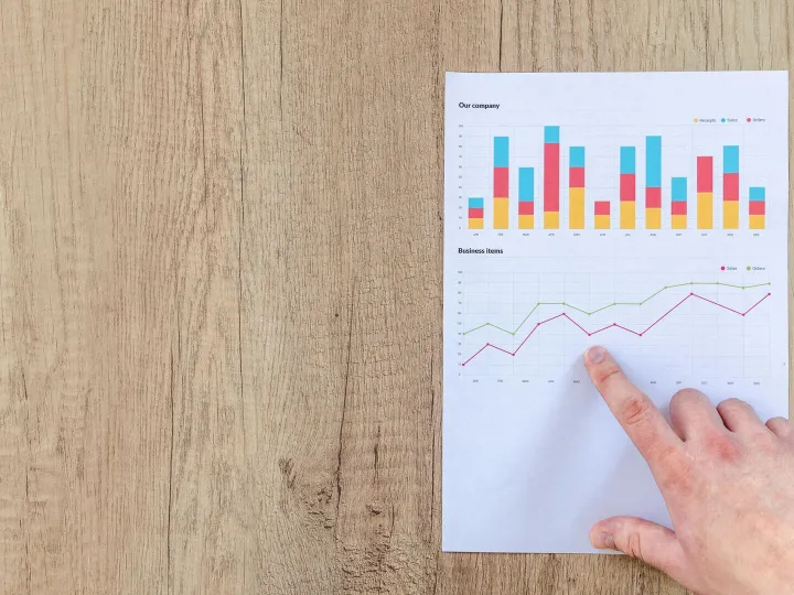 Hand analyzing business graphs on a wooden desk, f