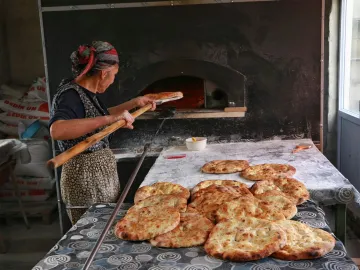Woman baking traditional bread in a rustic kitchen with a wood-fired oven.