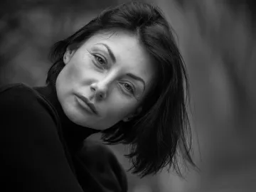 Black and white portrait capturing the intense gaze of a woman in a serene outdoor setting.