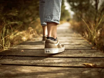 Person wearing sneakers walking on a wooden path