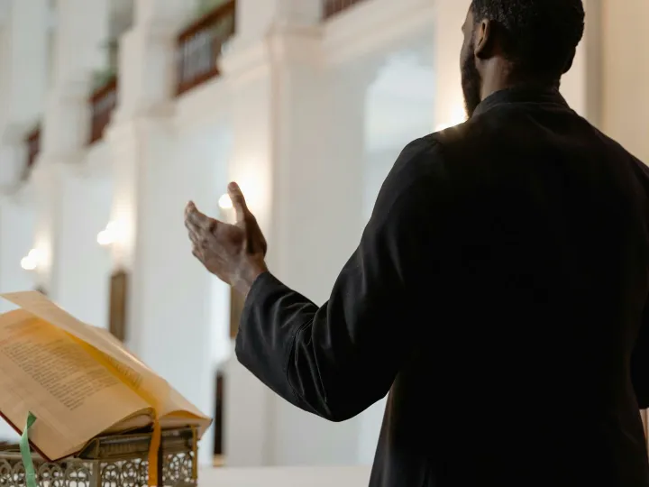 A priest delivers a sermon inside a beautifully lit church, standing at an altar.