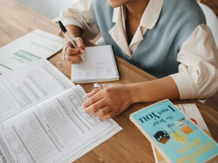 A person studying at a desk with books and a notepad, focusing on handwritten notes.
