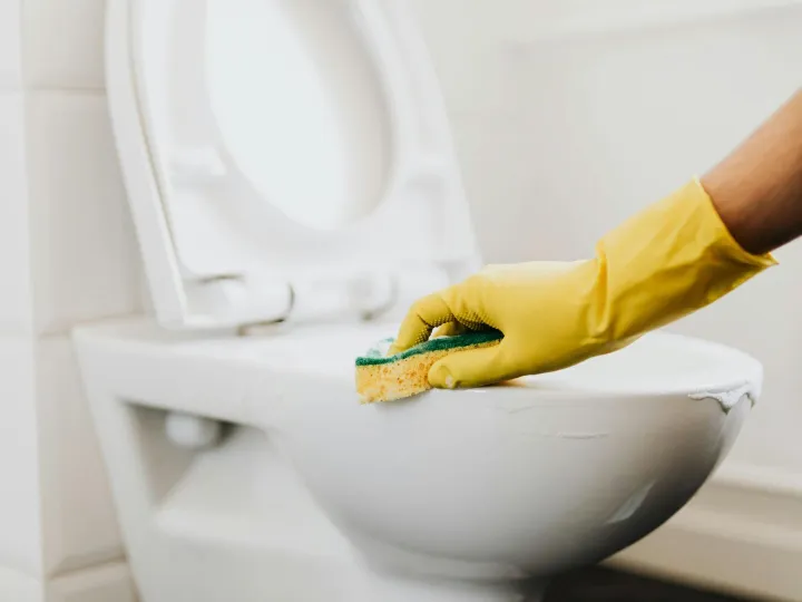 A close-up of a hand in a yellow glove cleaning a 